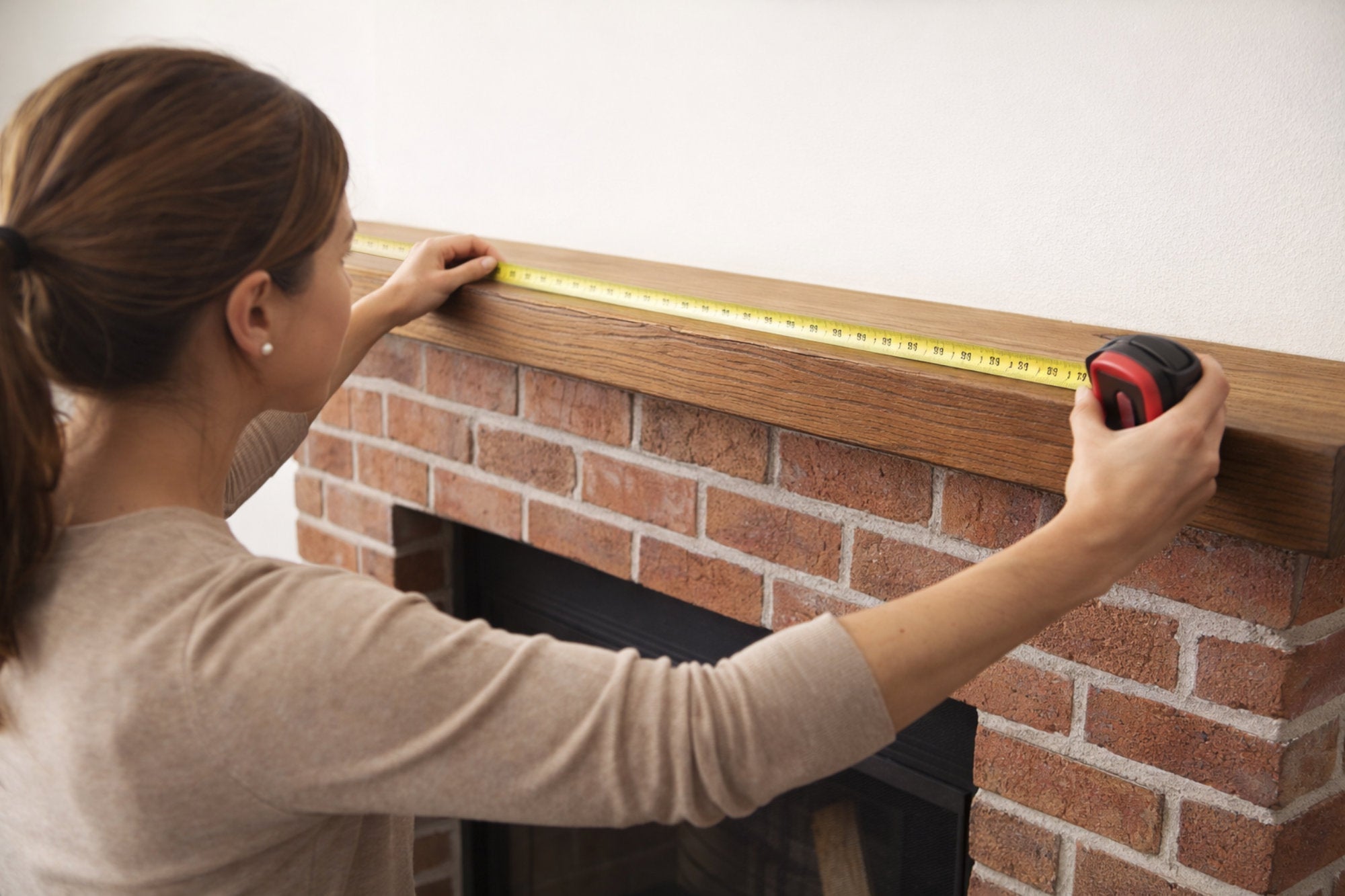 Woman measuring the length of a fireplace mantel with a tape measure